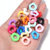 A hand holds a collection of colorful doughnut-shaped acrylic spacer beads for jewelry making.