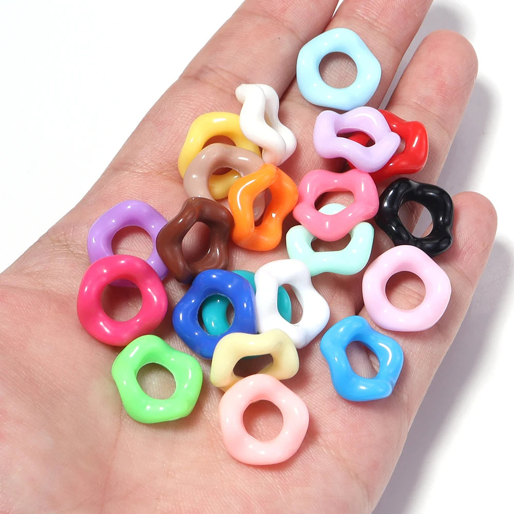 A hand holds a collection of colorful doughnut-shaped acrylic spacer beads for jewelry making.