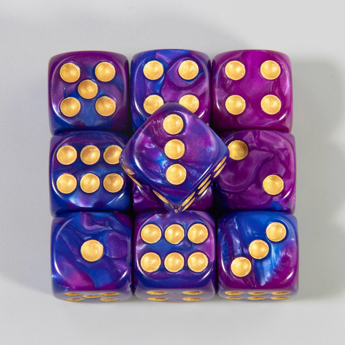 A set of ten multicolor acrylic dice with rounded corners and gold dots, arranged in a row.