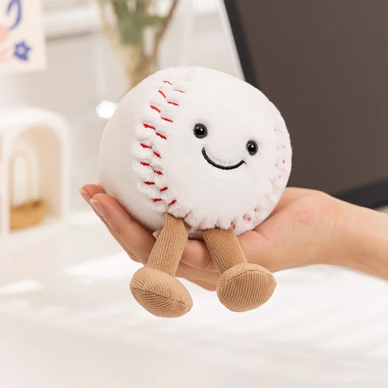 A hand holds a white plush sports ball companion with stitched seams and small feet.