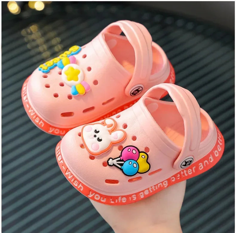 A pink lightweight children's clog with yellow and orange decorations is held in a hand.