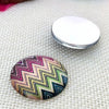A round craft doll eye with a multicolored chevron pattern and glitter finish resting on a silver metal disc.