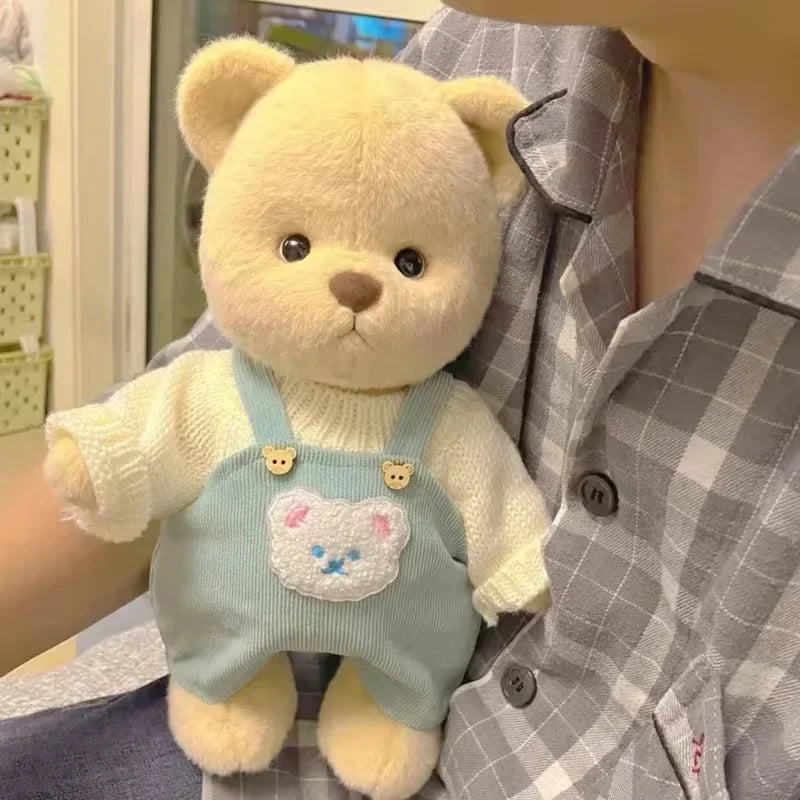A yellow teddy bear plush wearing a light blue overalls with a white bear face design.