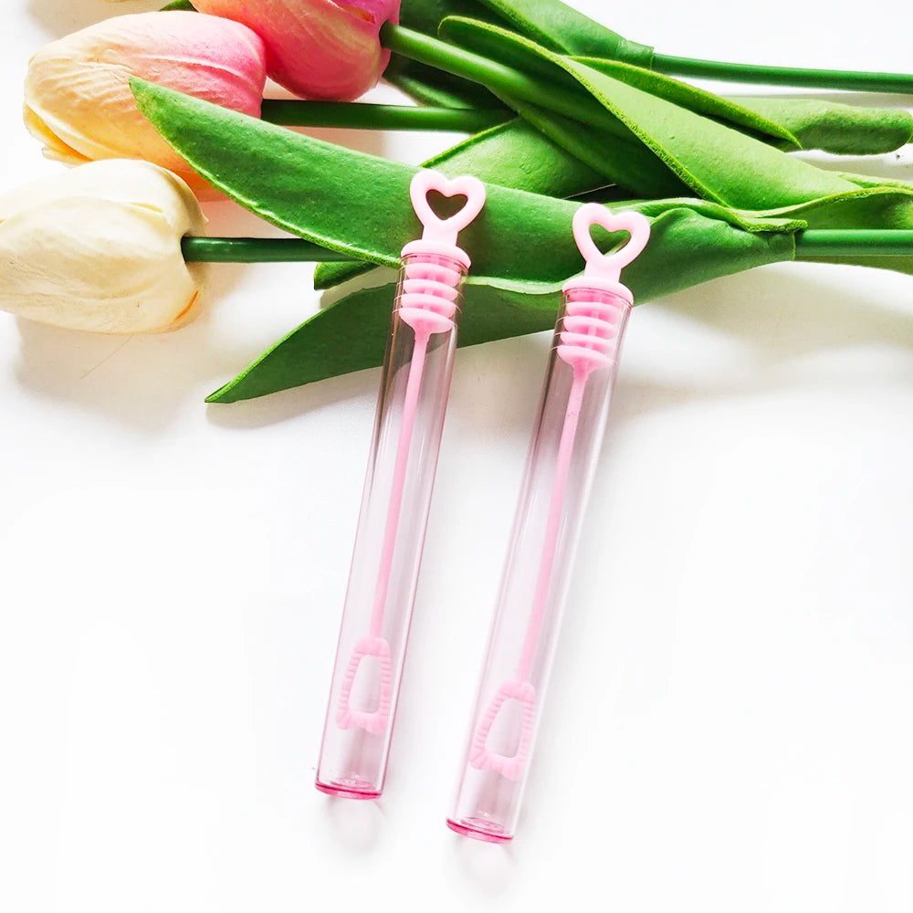 Two pink mini bubble wands with loop handles are displayed on green leaves and tulips.