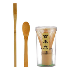 A set of traditional bamboo matcha whisks, including a long stick and a round spoon, displayed in a glass container.