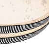 A close-up view of a light-colored drum shell with a black patterned strap and small dots on the surface.