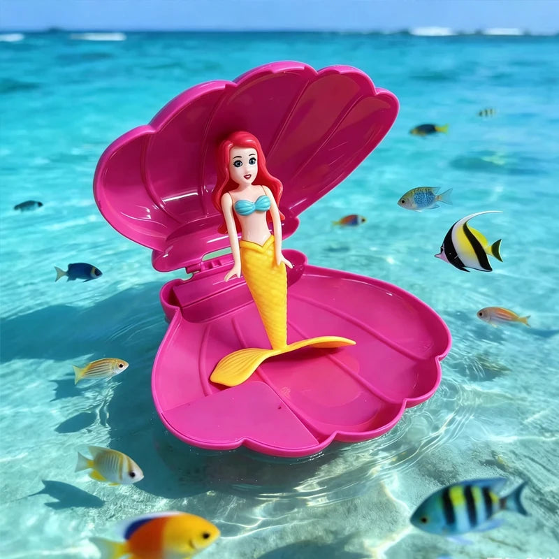 A mermaid figurine with pink tail floats in clear blue water surrounded by small tropical fish.