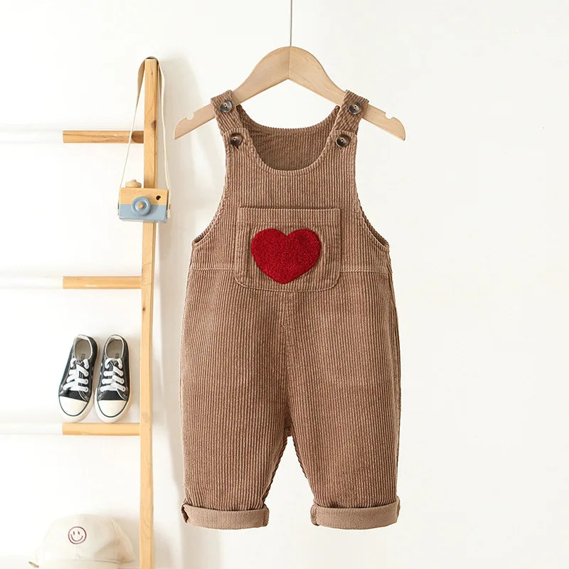 Toddler corduroy overalls in brown with a red heart embroidery hanging on a wooden hanger.
