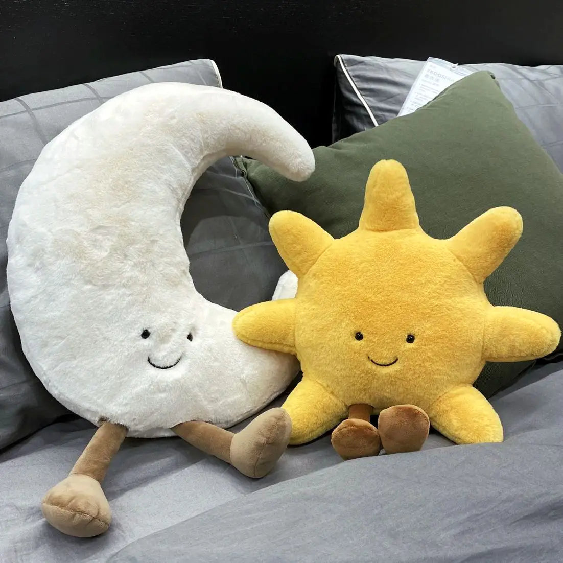 A plushie set featuring a yellow sun and a white crescent moon resting on a gray bedding surface.