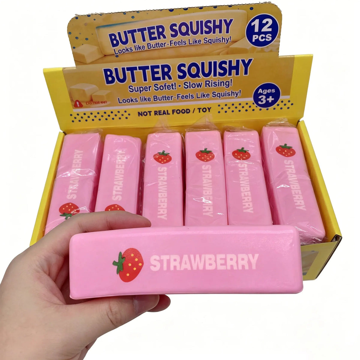 A hand holds a pink squishy strawberry stress relief toy from a box labeled Butter Squishy.