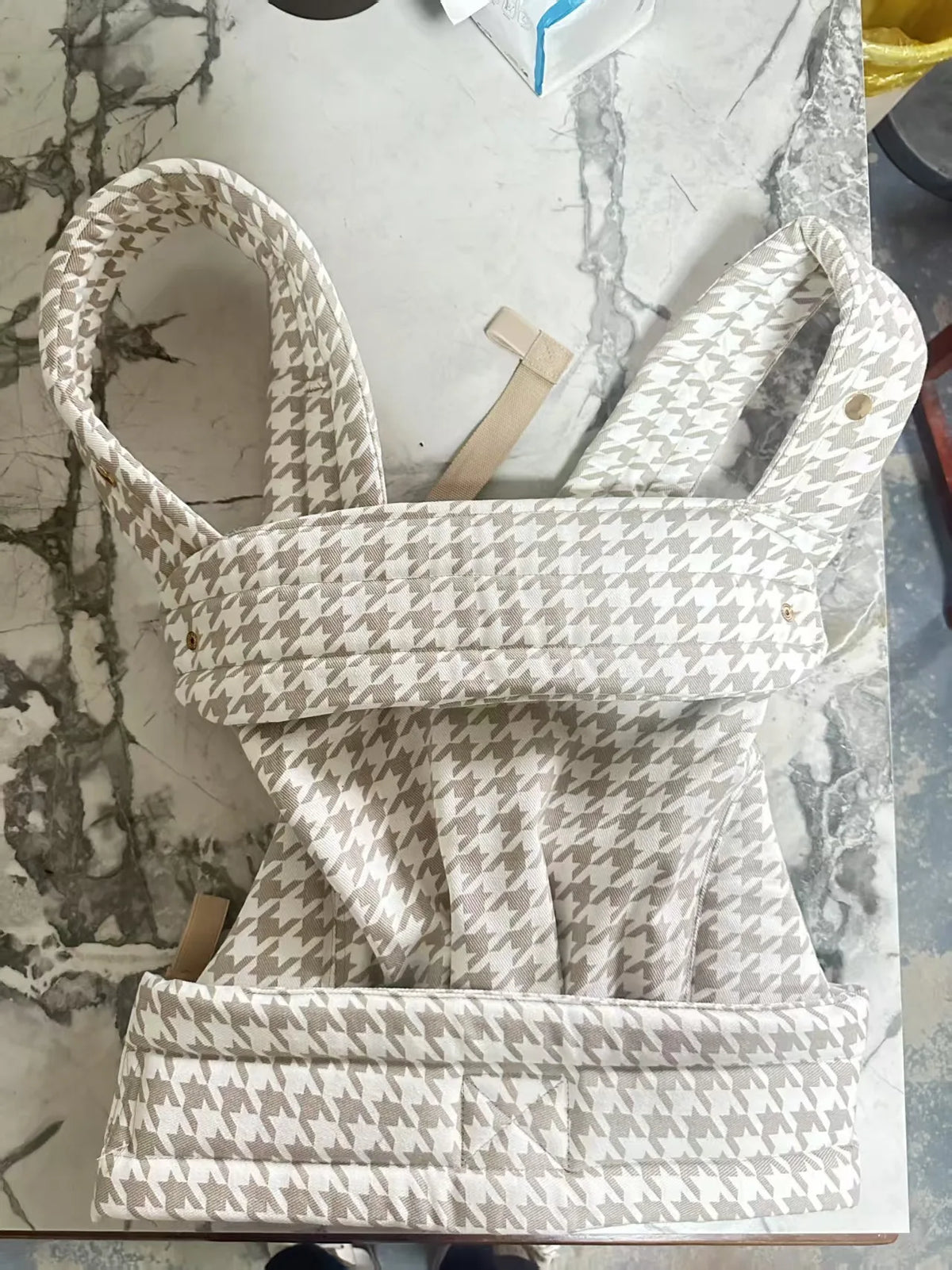 A white and gray patterned adjustable cotton baby carrier wrap displayed on a marble surface.