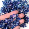 A hand holds a cluster of deep blue iridescent acrylic beads shaped like four-petal flowers for jewelry making.