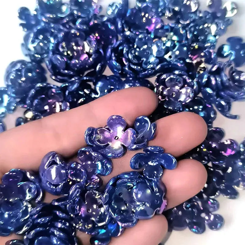 A hand holds a cluster of deep blue iridescent acrylic beads shaped like four-petal flowers for jewelry making.