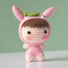 A handmade crochet doll kit featuring pink skin, brown hair, and green ears.