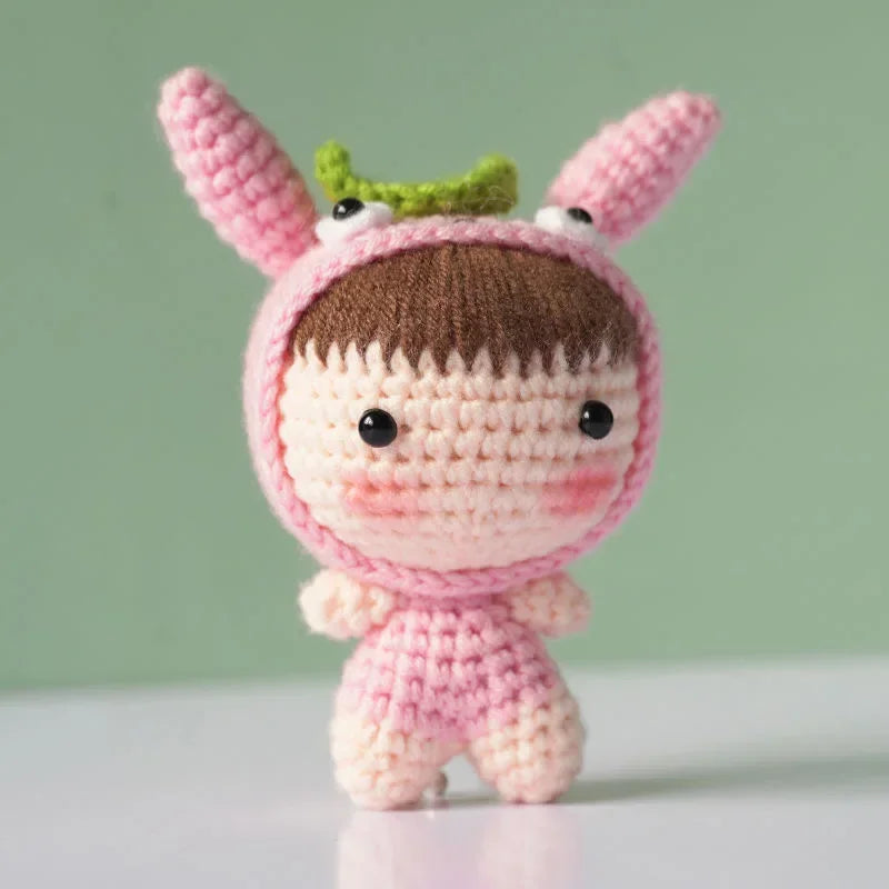 A handmade crochet doll kit featuring pink skin, brown hair, and green ears.