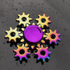 A colorful metal fidget spinner featuring a central purple disc surrounded by eight golden-yellow blades.
