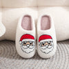 Pair of white plush indoor slippers with Santa face embroidery resting on a textured gray surface.