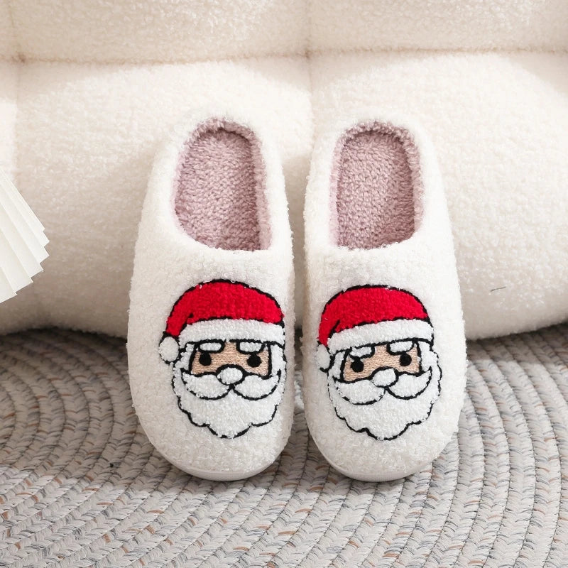 Pair of white plush indoor slippers with Santa face embroidery resting on a textured gray surface.