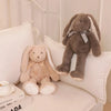 A soft gray bunny plush toy with long ears and a bow is resting on a white pillow.