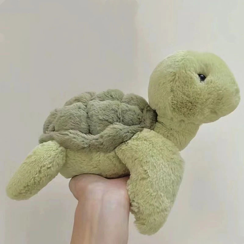 A light green simulated turtle plush doll is being held by a person's hand.