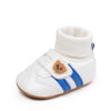 White baby booties with blue stripes and a tan pom-pom detail