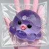 A purple squishy bubble squid stress relief toy is held in a person's hand inside a clear plastic bag.