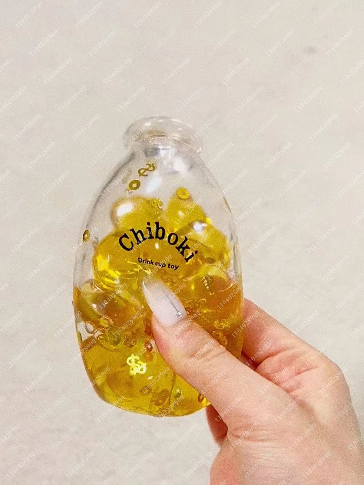 A hand holds a clear glass bottle filled with yellow liquid and several yellow squishy stress balls labeled Chiboki.