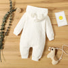 A white knitted hooded baby romper lying on a wooden surface next to a small ball and a smiling emoji card.