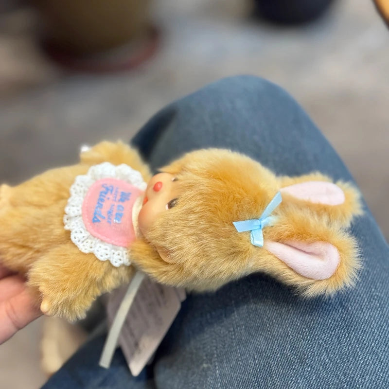 A fluffy orange rabbit plush toy with pink ears and a small heart tag is held in a person's hand.