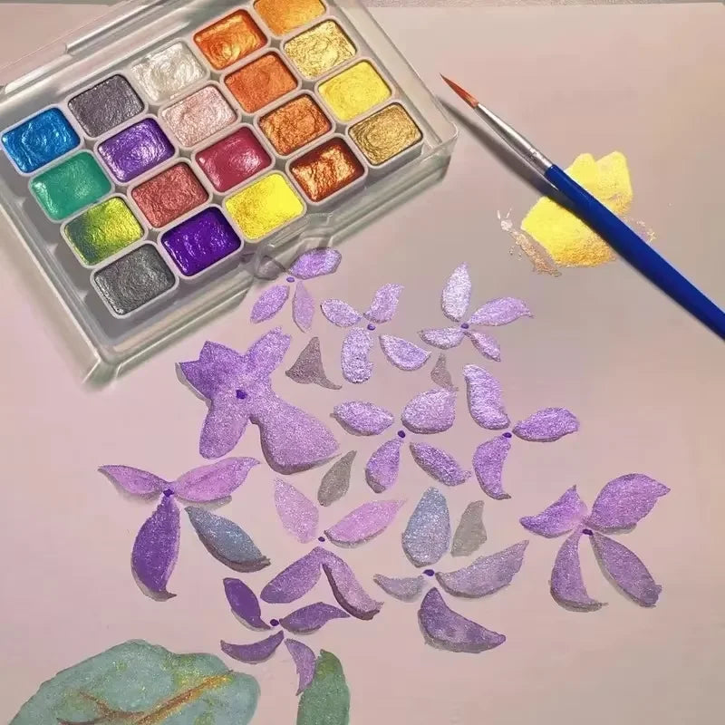 A palette of 20 metal watercolor paints with pearl finish alongside purple floral cutouts.