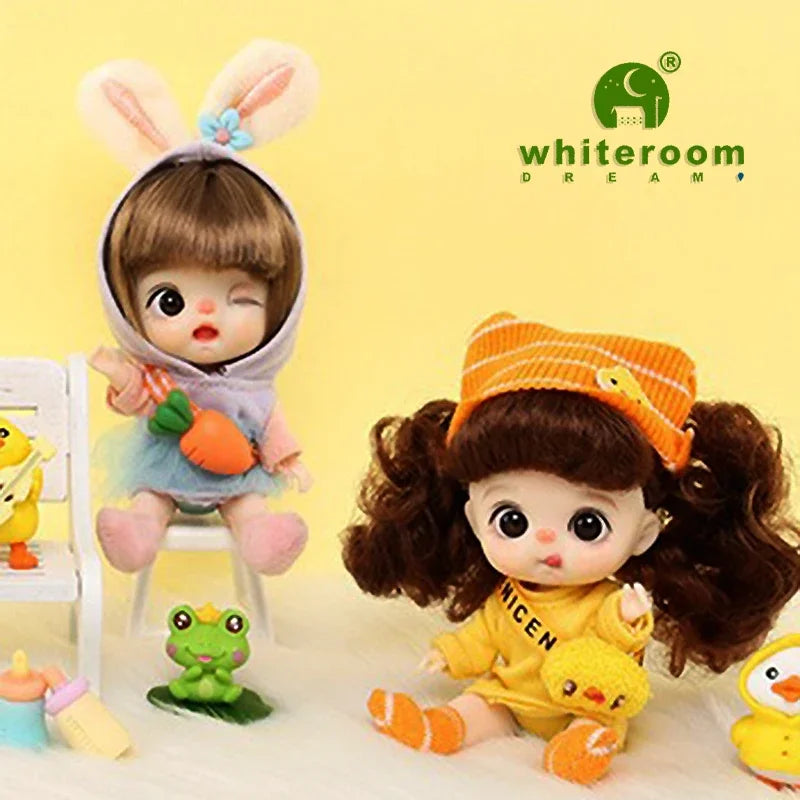A small, brown-haired doll with curly hair and large eyes is shown next to a yellow orange headband and yellow clothing.