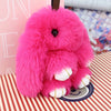 A bright pink plush bunny keychain with a black nose and white inner ears resting on a patterned surface.