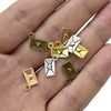 A hand holds a collection of vintage gold and silver envelope charms for jewelry making.