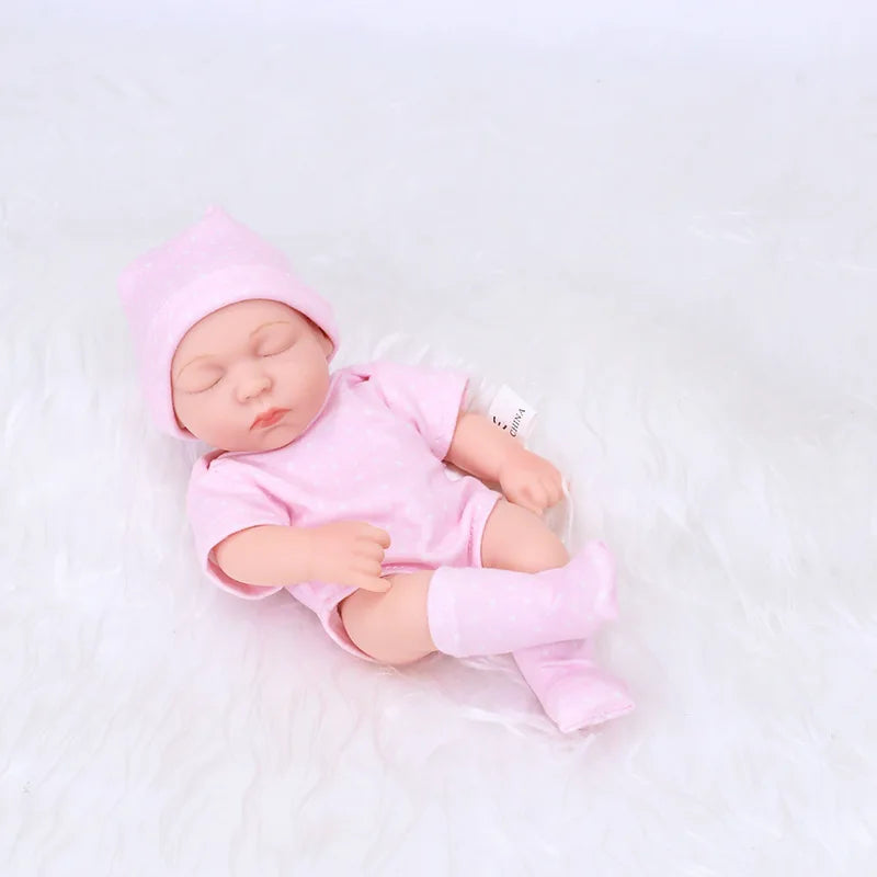 A realistic soft vinyl baby doll wearing a pink outfit and hat, lying on a white surface.