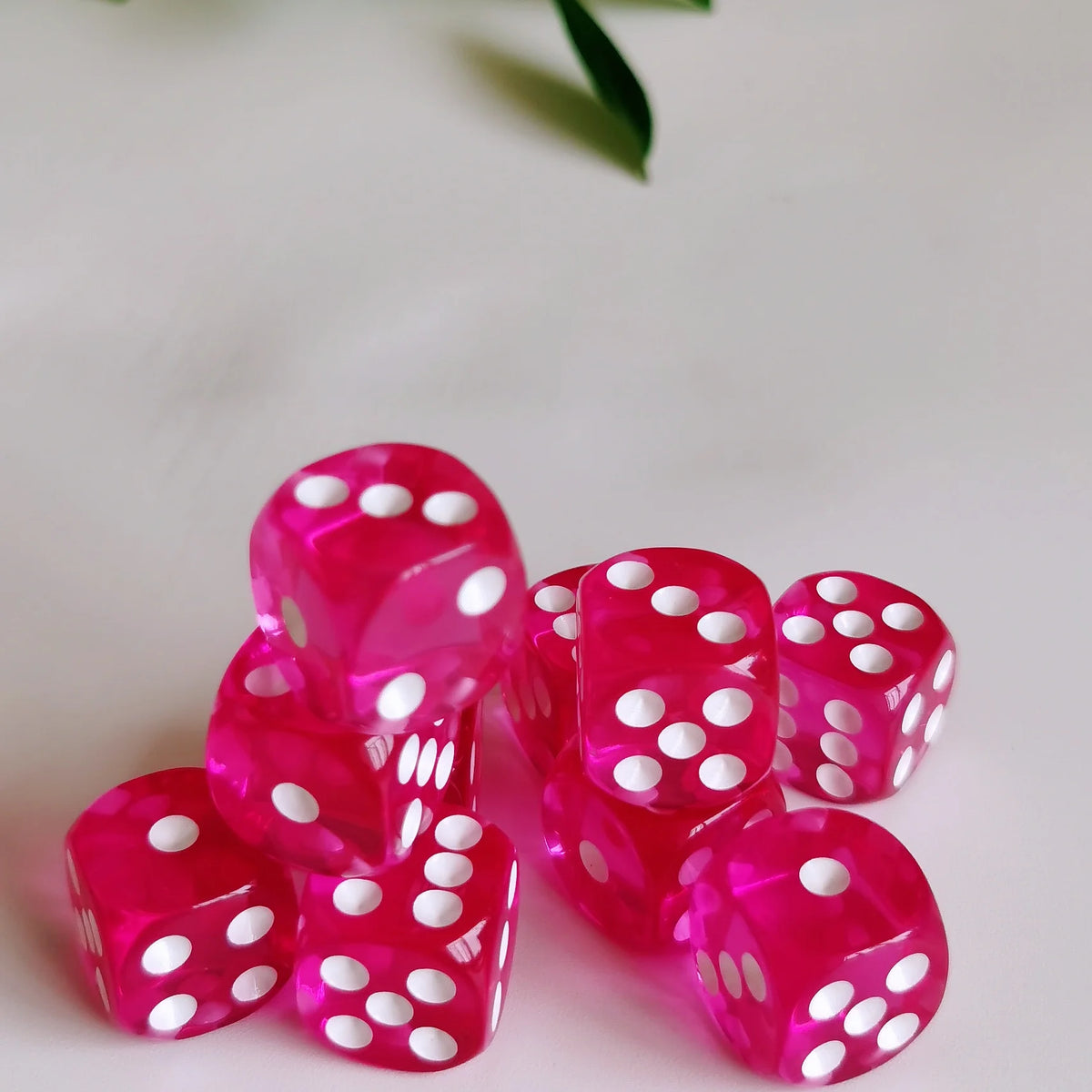 A close-up of a pile of bright pink transparent dice with white dots on a white surface.