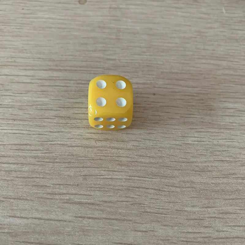 A single yellow solid acrylic die with five dots is placed on a light wooden surface.