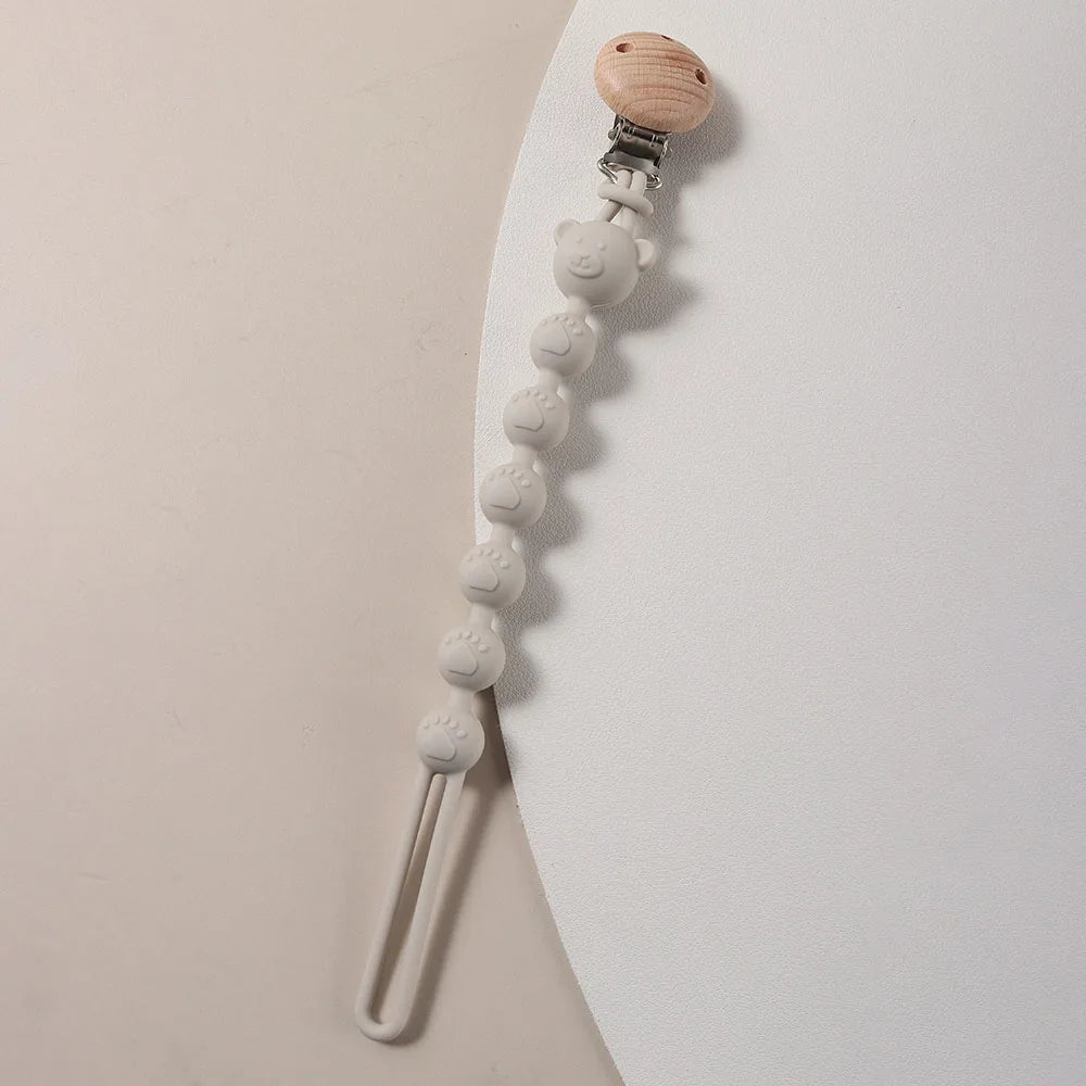 A silicone bear paw pacifier clip with a wooden top and a metal clip attached to a chain.