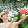 A young girl is playing with a red and green pull-string flying saucer launcher toy outdoors.