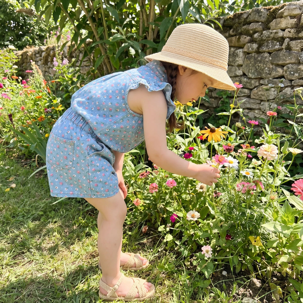 A young girl wearing a light blue floral print sleeveless shirt and shorts set in a garden.