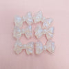A set of translucent, shimmering mermaid-inspired bowknot beads for jewelry making arranged on a pink surface.