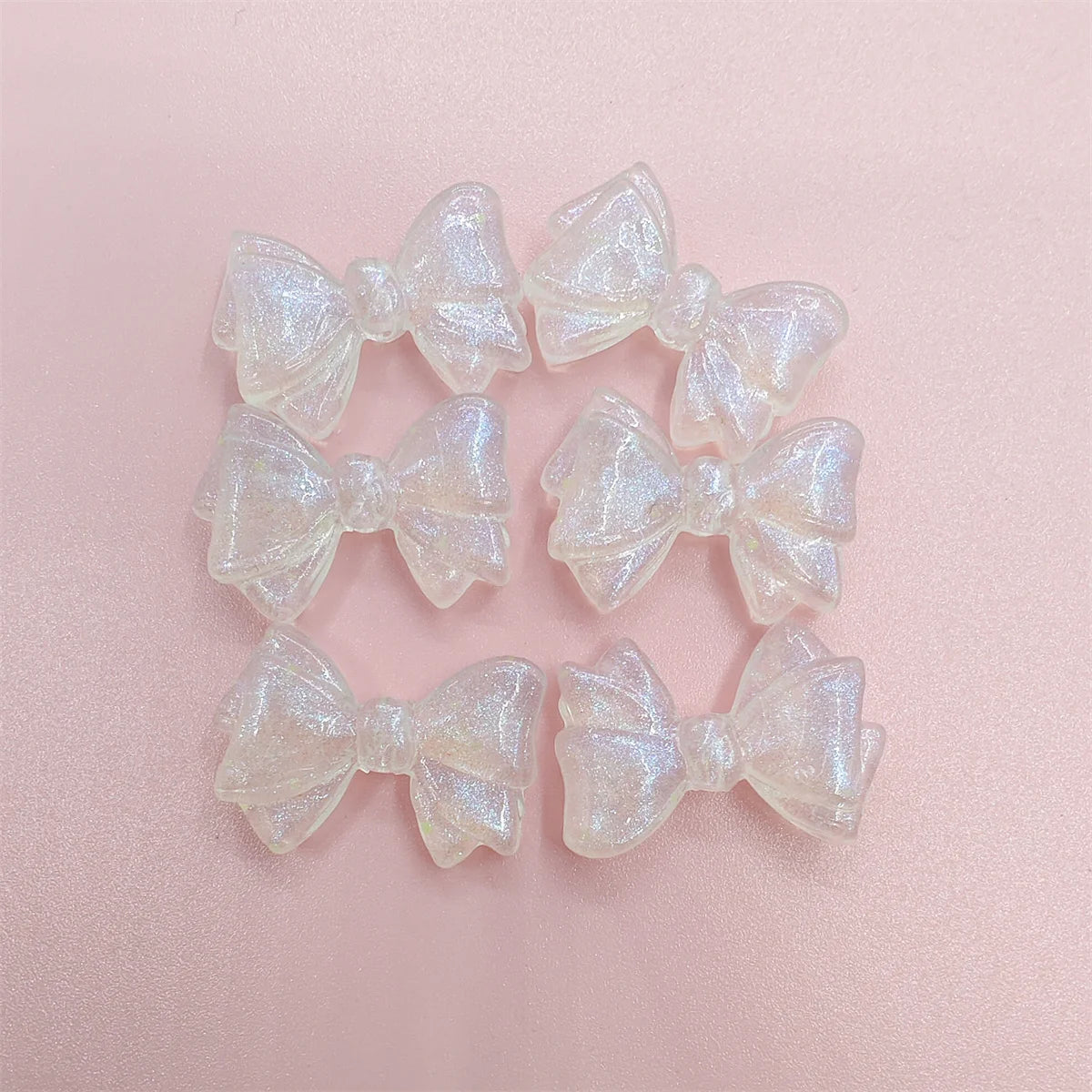 A set of translucent, shimmering mermaid-inspired bowknot beads for jewelry making arranged on a pink surface.