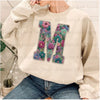 A light beige sweatshirt featuring a large embroidered floral letter M on the chest.