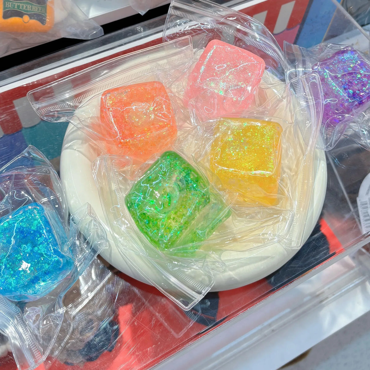A clear plastic container holds several square, translucent fidget toys in various colors including orange, pink, yellow, and
