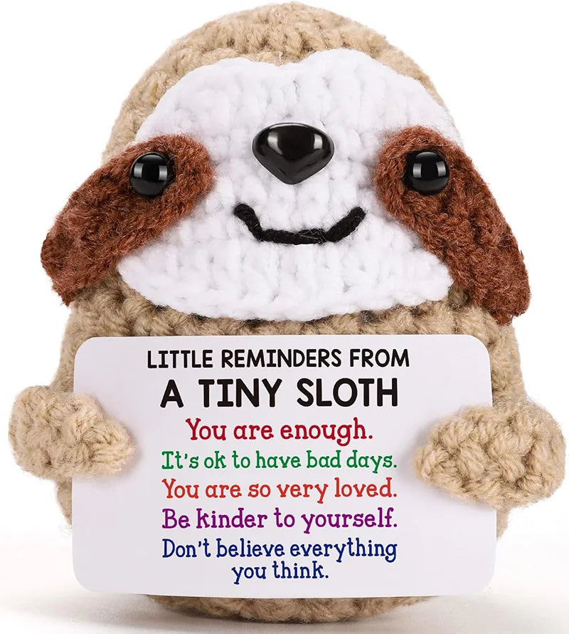 A handmade crochet plush sloth with brown and white fur, smiling, featuring a positive message.