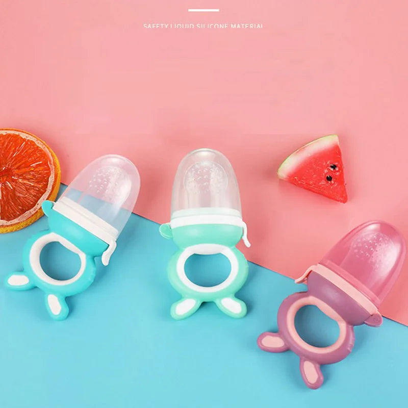 Pink and teal silicone baby food feeder with teether shown against a pink background.
