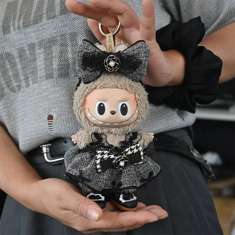 A small, fluffy doll wearing a black and white checkered outfit with a bow is held in a person's hand.