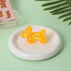 A bright orange translucent stress ball squishy toy resting on a white plate with a green background.