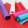 A collection of rolled crepe paper in various colors including purple, pink, red, and teal on a red background.
