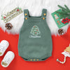A green knit baby romper with Christmas embroidery lies on a red background surrounded by white boots and pine greenery.