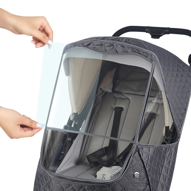 A gray waterproof stroller cover with a clear window showing the interior and a hand adjusting it.